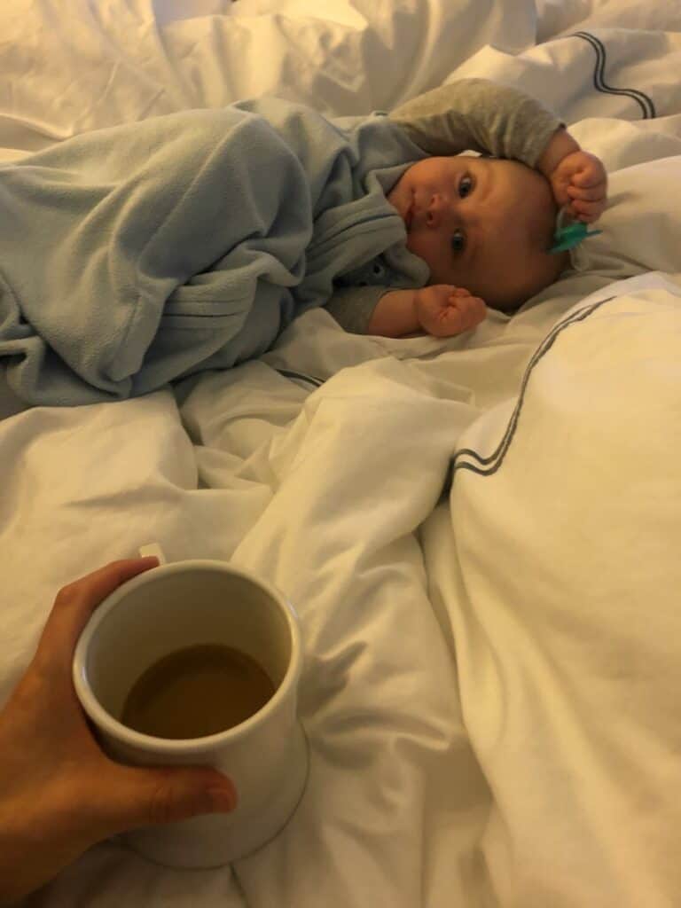 Jacob laying in bed and Lindsey holding her cup of coffee