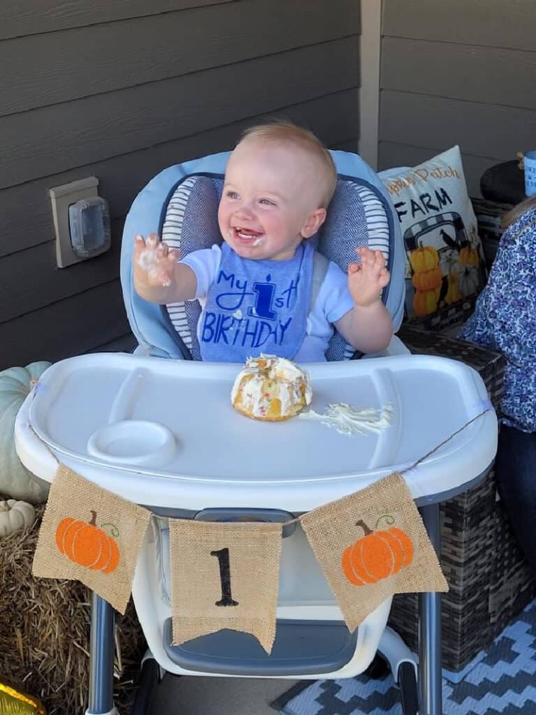 Jacob with a big smile and his hands in the air as he eats his cake.