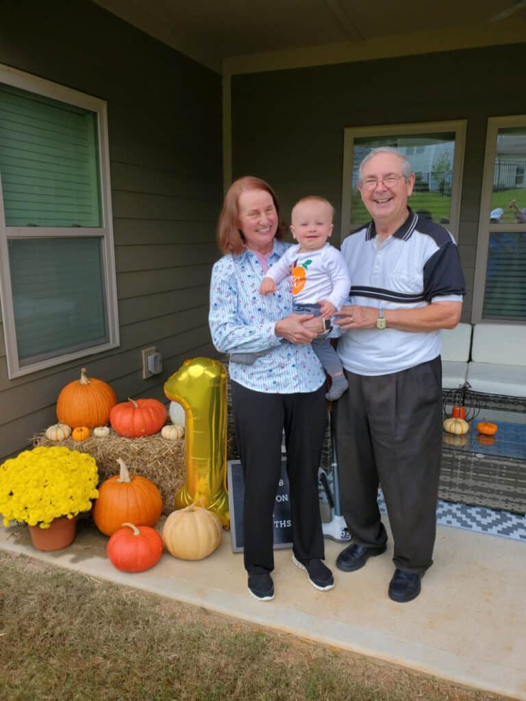 Jacob smiling with Mimi & Papa by his highchair outside. 