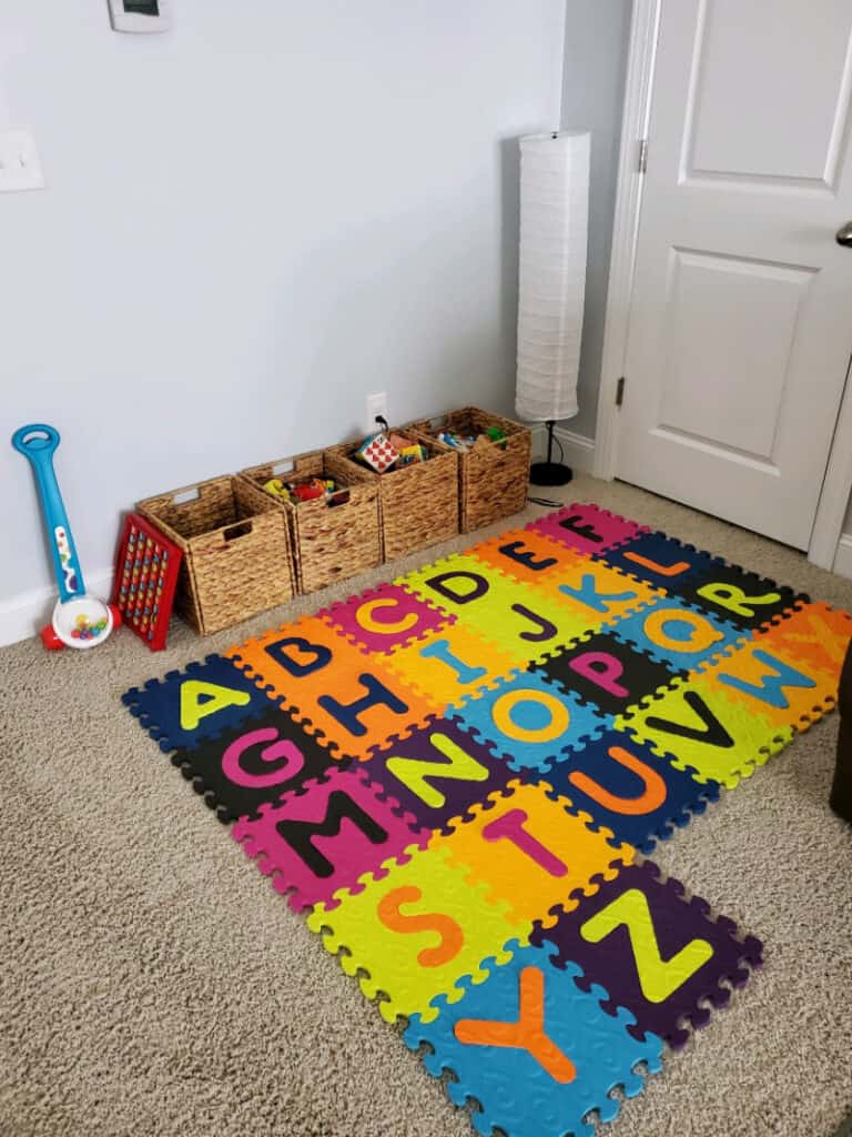 Alphabet mat and cubes lined up against the wall full of toys. 