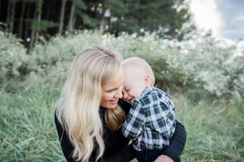 Jacob and Lindsey family photo outside. He is nuzzled up smiling as she looks towards him.