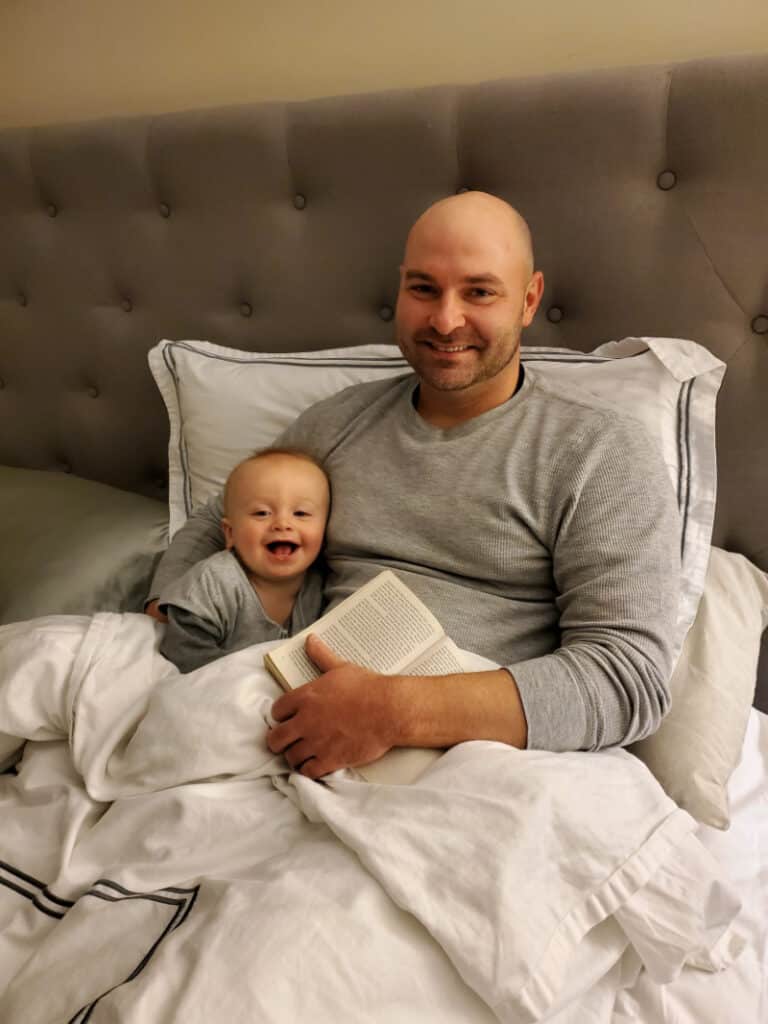 Jacob smiling big with Daddy reading in bed.