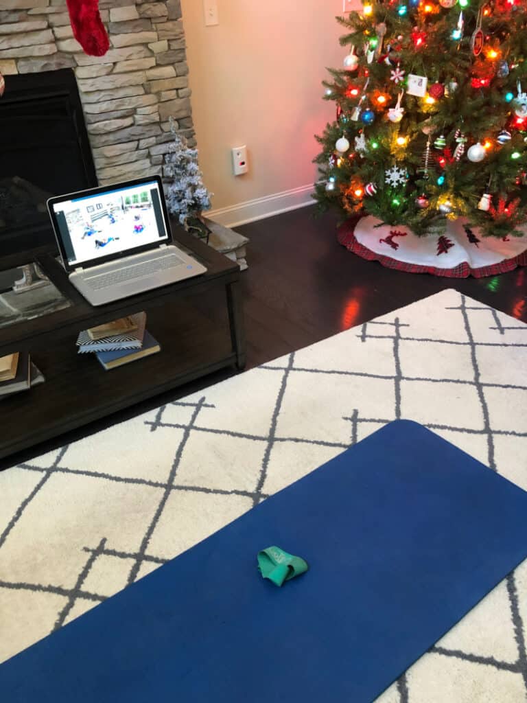 The laptop set up on the coffee table by the Christmas tree and a yoga mat on the floor.