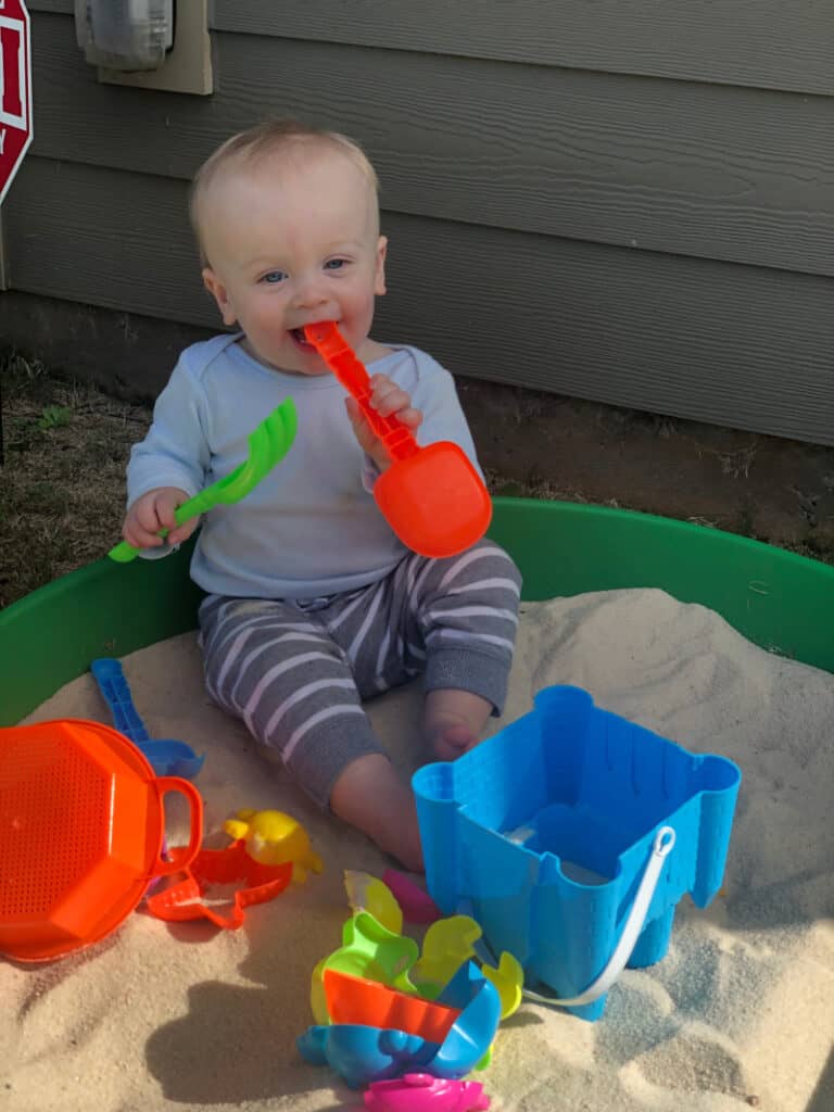 Jacob in the sandbox with a shovel in his mouth.