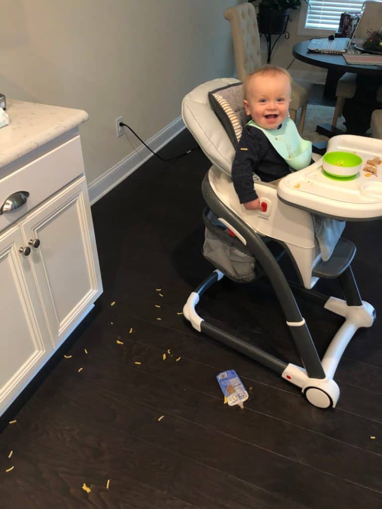 Jacob smiling in his highchair about all the food he threw on the floor